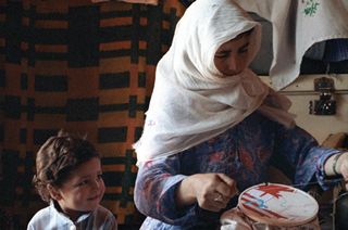 #P5.4.june90 A child looks on as his mother stitches a Mappa. The mother holds her veil in her teeth to keep it from slipping while she is being photographed.,Randi Malkin Steinberger